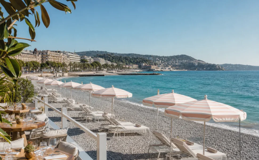 A refined private beach setup with pastel parasols and sun loungers beside the Mediterranean Sea in Nice.